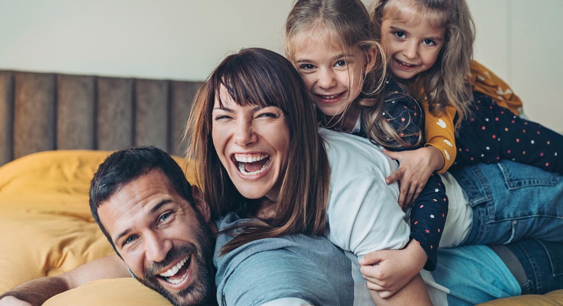 Vater, Mutter und zwei Töchter toben lachend auf dem Bett